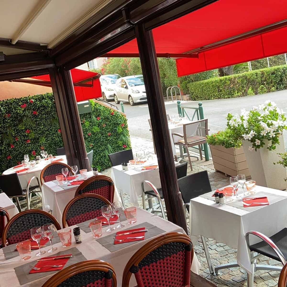 La terrasse couverte sous son auvent rouge, tables dressées et fauteuils de bistrot